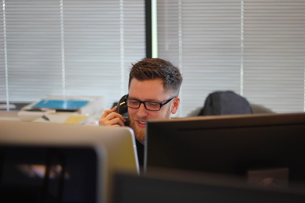 A man speaks on the phone while seated at a computer, focusing on efficient customer service operations.